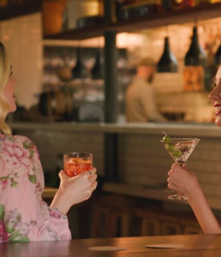 Two Women Stand with Drinks in Hand