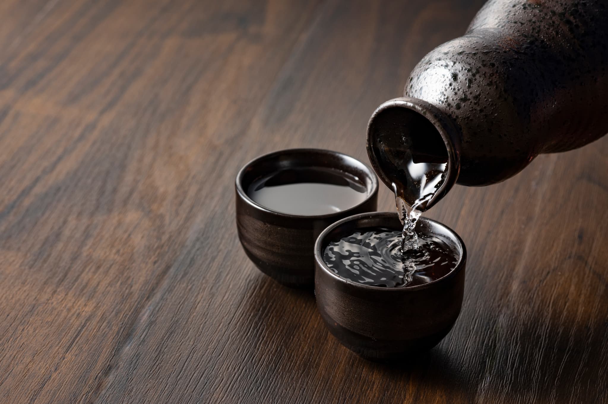 Two small round cups being filled with sake